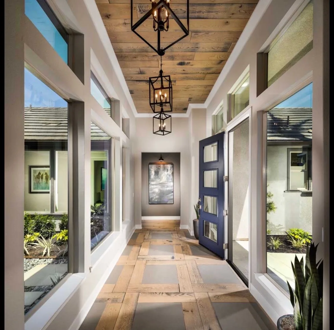 Bright entry hall with a wood-inlay floor, navy blue front door, and exposed wood ceiling.